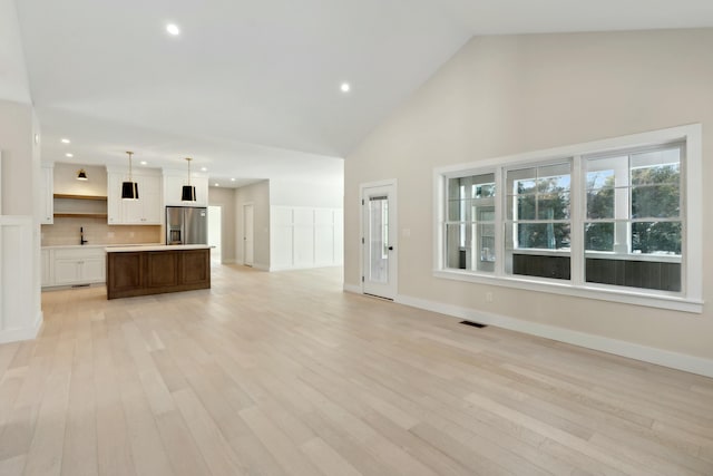 unfurnished living room featuring sink, light hardwood / wood-style flooring, and high vaulted ceiling