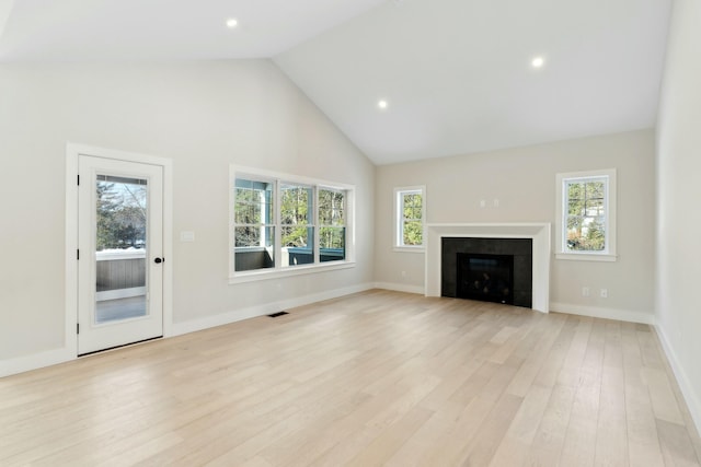 unfurnished living room featuring a tiled fireplace, a wealth of natural light, and light wood-type flooring