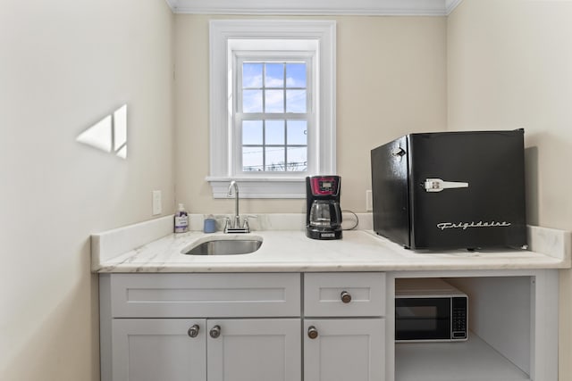 interior space with white cabinetry, crown molding, sink, and light stone counters