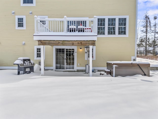 snow covered back of property featuring a hot tub and a balcony