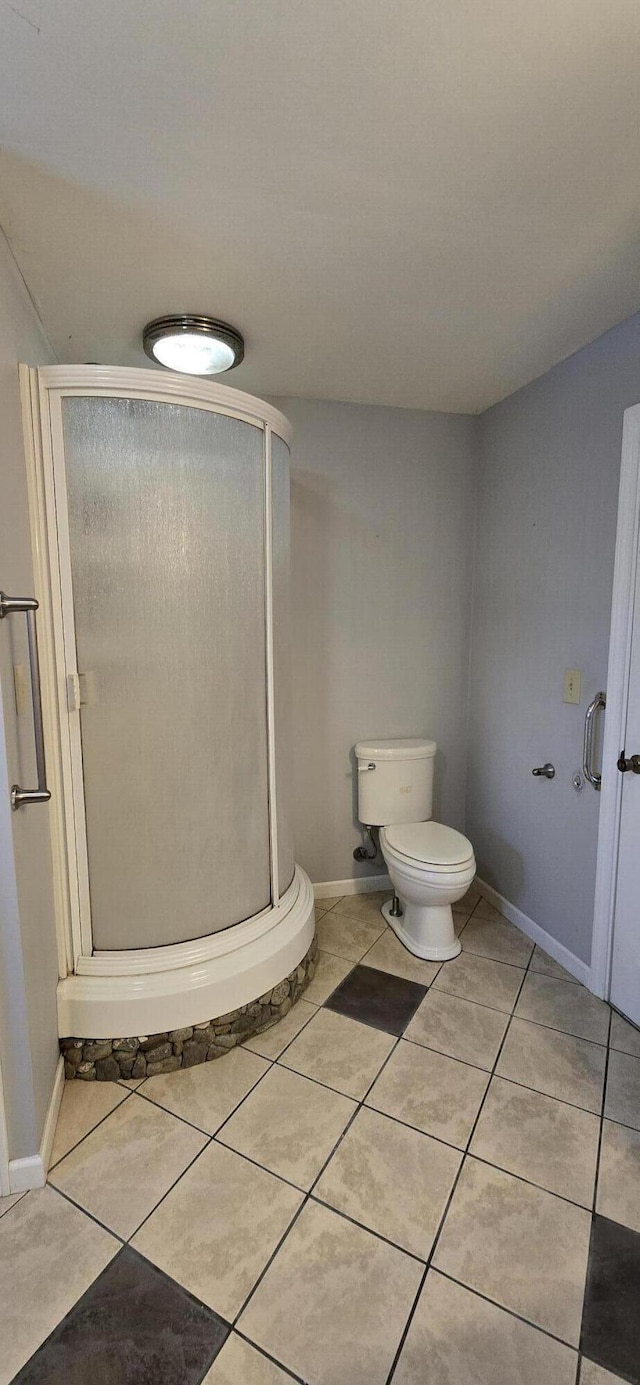 bathroom featuring toilet, a shower with door, and tile patterned flooring