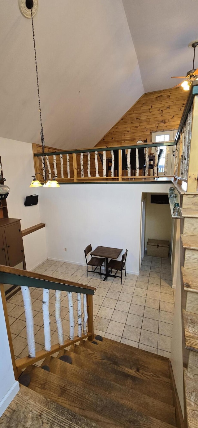 stairway with ceiling fan, tile patterned floors, wood walls, and lofted ceiling