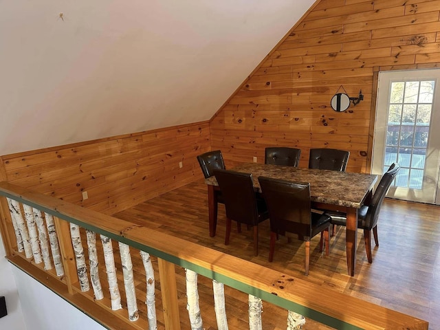 dining area featuring lofted ceiling, hardwood / wood-style floors, and wood walls