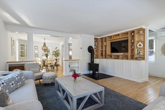 living room featuring hardwood / wood-style flooring, a wall mounted AC, decorative columns, and a wood stove