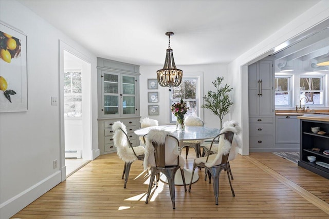 dining space with sink, a baseboard heating unit, a chandelier, and light wood-type flooring