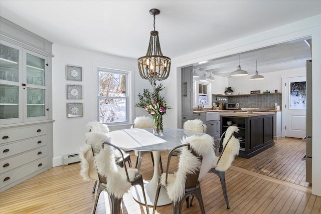 dining area featuring baseboard heating, sink, light hardwood / wood-style flooring, and a notable chandelier