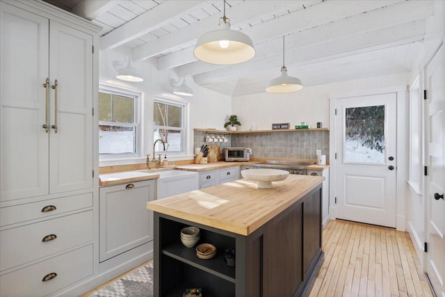 kitchen featuring white cabinetry, butcher block counters, sink, hanging light fixtures, and beam ceiling