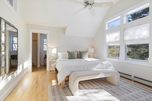 bedroom with vaulted ceiling, a walk in closet, a baseboard heating unit, ceiling fan, and light hardwood / wood-style flooring