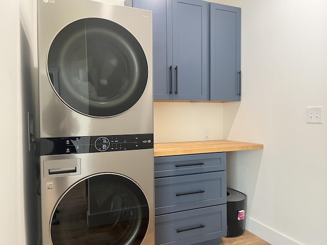 laundry area with stacked washer and dryer, light hardwood / wood-style floors, and cabinets