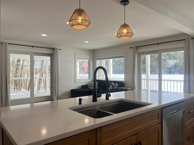 kitchen with light stone countertops, sink, stainless steel dishwasher, and decorative light fixtures