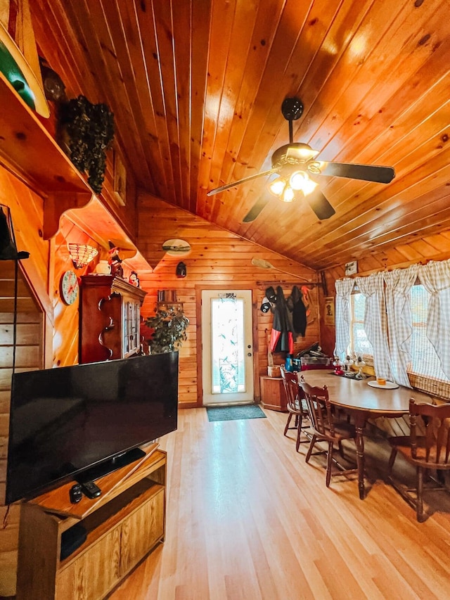 dining room featuring wood walls, lofted ceiling, ceiling fan, wood ceiling, and light hardwood / wood-style flooring