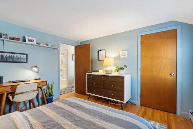 bedroom featuring a baseboard heating unit, hardwood / wood-style floors, and ensuite bathroom