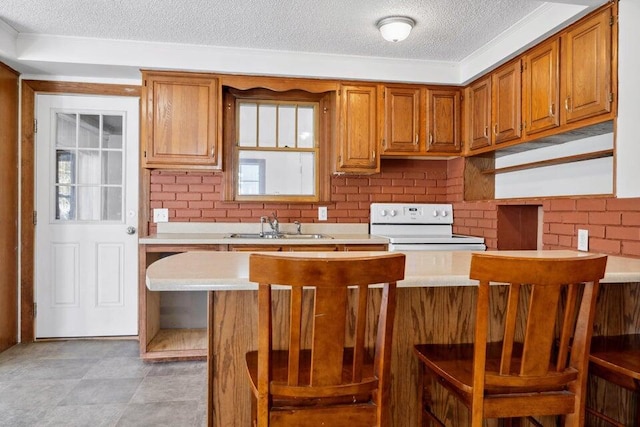 kitchen featuring a breakfast bar, sink, a textured ceiling, and white range with electric stovetop