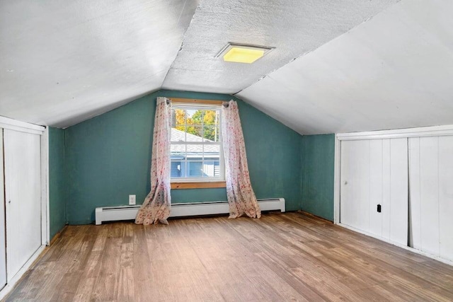 additional living space with vaulted ceiling, a baseboard heating unit, a textured ceiling, and light hardwood / wood-style floors