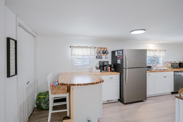 kitchen with sink, white cabinets, wooden counters, stainless steel appliances, and light hardwood / wood-style flooring