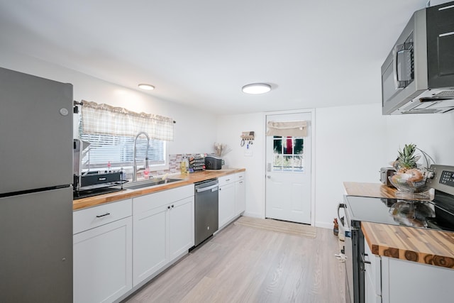 kitchen featuring sink, butcher block countertops, light wood-type flooring, stainless steel appliances, and white cabinets