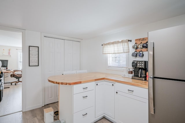 kitchen featuring wood counters, white cabinets, stainless steel fridge, kitchen peninsula, and light wood-type flooring