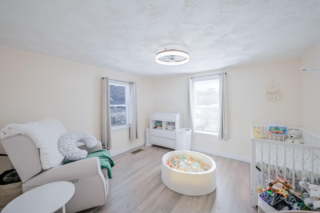 bedroom with a nursery area, light hardwood / wood-style flooring, and a textured ceiling