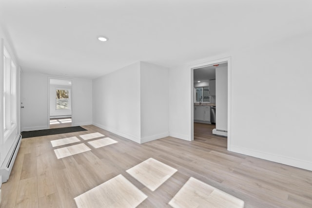 empty room with baseboards, baseboard heating, light wood-style flooring, and a baseboard radiator