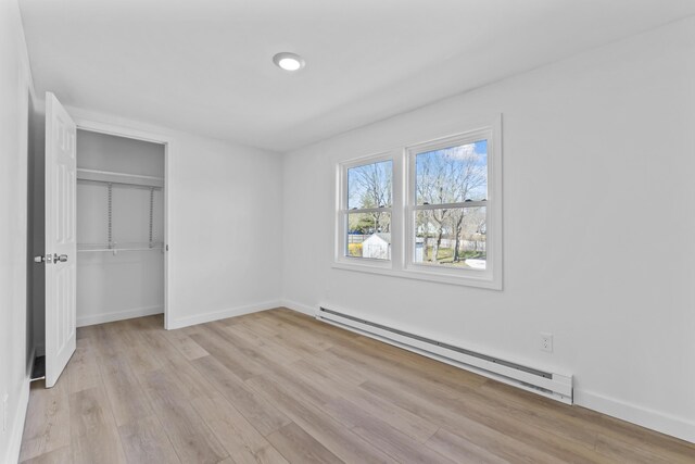 unfurnished bedroom featuring a closet, baseboards, light wood-style flooring, and a baseboard heating unit
