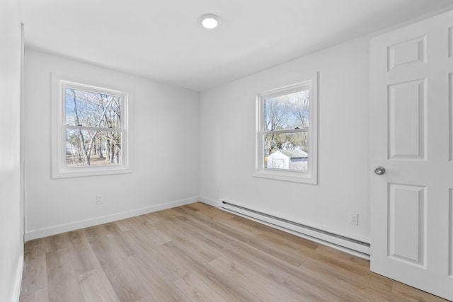 empty room with baseboards, a baseboard heating unit, and light wood-style floors