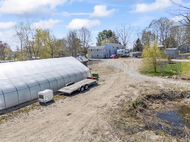 exterior space featuring dirt driveway, an outbuilding, and a greenhouse