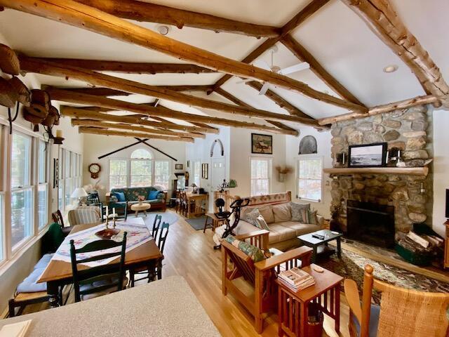 living room with light wood-type flooring, vaulted ceiling with beams, a fireplace, and plenty of natural light