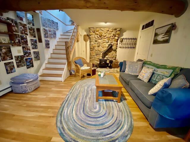 living room featuring beamed ceiling, wood-type flooring, and a wood stove