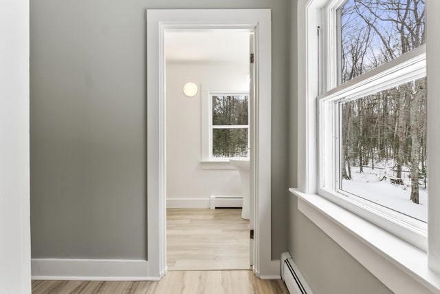 hall with a baseboard heating unit, a wealth of natural light, and light hardwood / wood-style floors