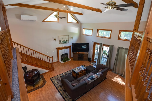 living room with ceiling fan, hardwood / wood-style floors, beam ceiling, a wall mounted AC, and a tiled fireplace