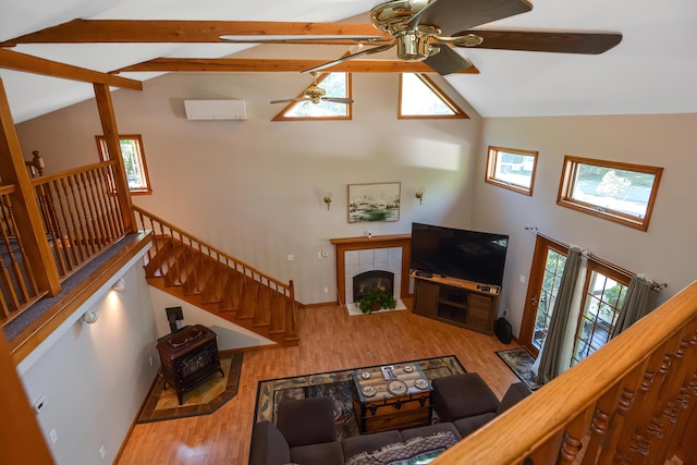 living room with high vaulted ceiling, a fireplace, ceiling fan, beam ceiling, and light hardwood / wood-style flooring