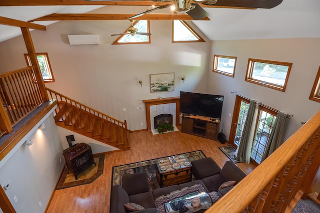 living room with high vaulted ceiling, a tiled fireplace, ceiling fan, beam ceiling, and light hardwood / wood-style flooring