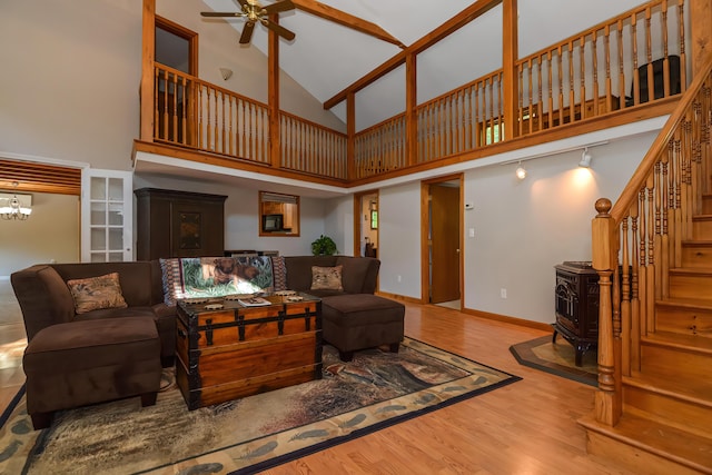 living room with hardwood / wood-style floors, ceiling fan with notable chandelier, a towering ceiling, and a wood stove