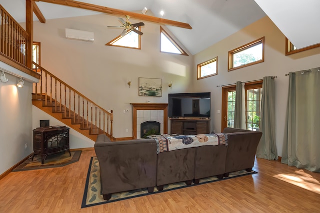 living room featuring a fireplace, a wall mounted AC, light wood-type flooring, ceiling fan, and beam ceiling