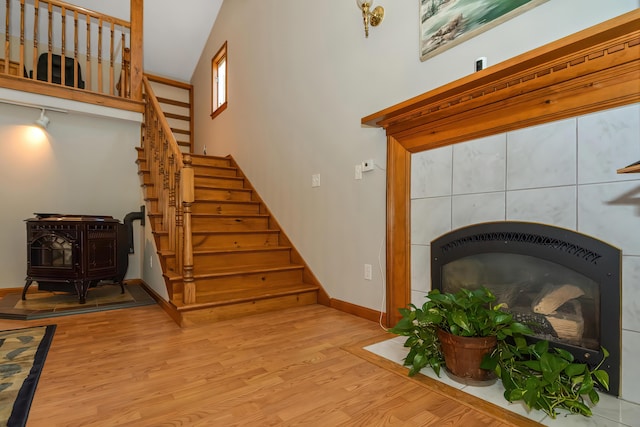 stairway with a wood stove, hardwood / wood-style floors, and a towering ceiling