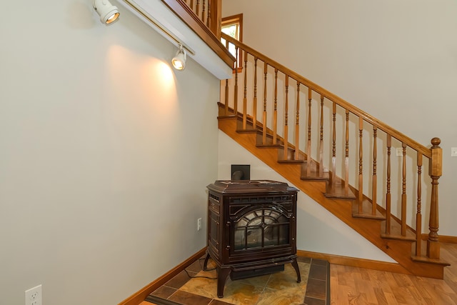 stairway with hardwood / wood-style flooring, rail lighting, and a wood stove