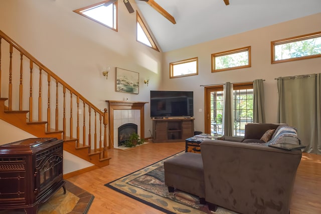 living room featuring high vaulted ceiling, hardwood / wood-style flooring, a tile fireplace, and ceiling fan