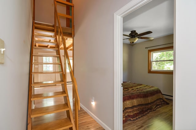 staircase with ceiling fan, a baseboard radiator, and hardwood / wood-style floors