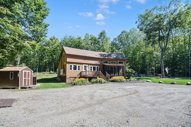 view of front of home featuring a wooden deck, a sunroom, a front lawn, and a storage shed