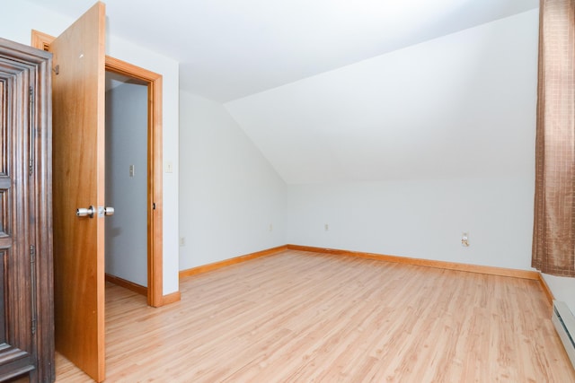 additional living space featuring a baseboard heating unit, vaulted ceiling, and light wood-type flooring