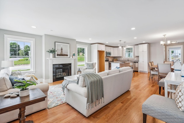 living room featuring sink, a wealth of natural light, a notable chandelier, and light wood-type flooring