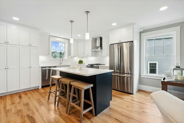 kitchen with decorative light fixtures, white cabinetry, a center island, stainless steel appliances, and wall chimney range hood