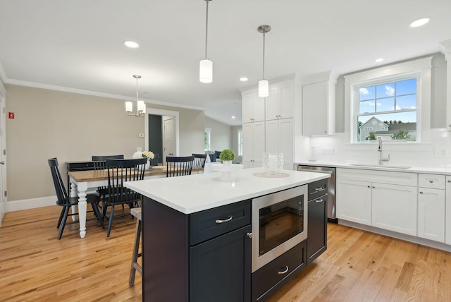 kitchen with appliances with stainless steel finishes, white cabinetry, hanging light fixtures, a kitchen island, and light wood-type flooring