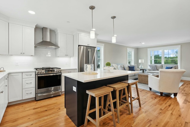 kitchen featuring white cabinetry, wall chimney range hood, stainless steel appliances, and a kitchen island