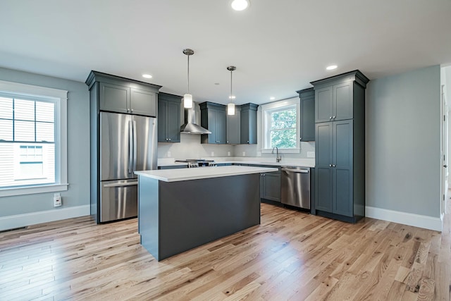 kitchen featuring pendant lighting, a center island, stainless steel appliances, wall chimney range hood, and light wood-type flooring