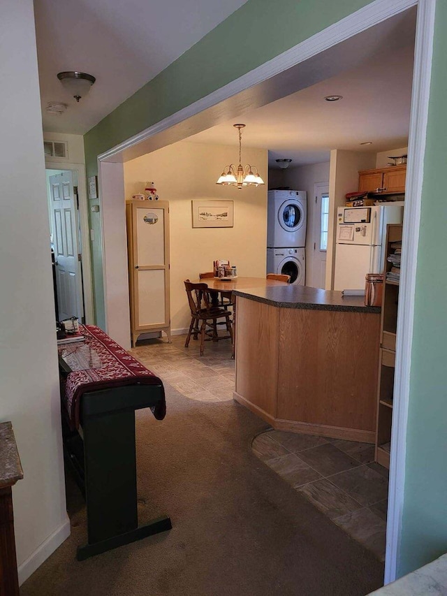 kitchen featuring stacked washing maching and dryer, white refrigerator, hanging light fixtures, a notable chandelier, and kitchen peninsula