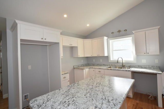 kitchen with lofted ceiling, sink, white cabinetry, a center island, and light stone counters