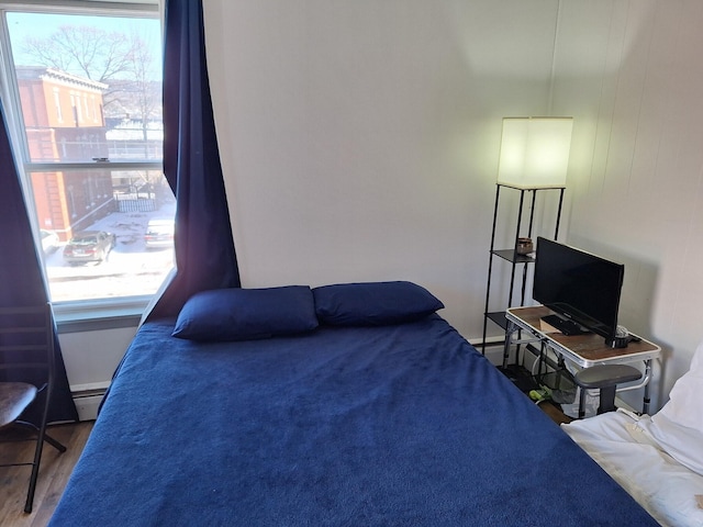 bedroom with multiple windows, hardwood / wood-style flooring, and baseboard heating