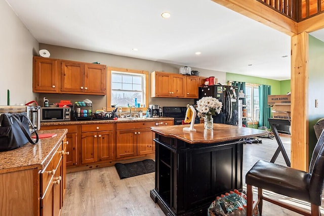 kitchen with sink, light stone counters, black appliances, a kitchen island, and light wood-type flooring