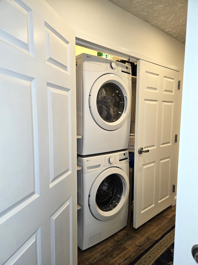 laundry room featuring dark wood-type flooring, a textured ceiling, and stacked washing maching and dryer